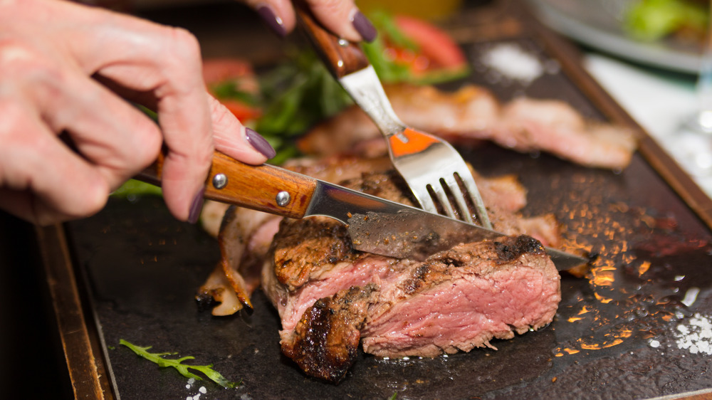 Hands cutting a steak with a fork and knife
