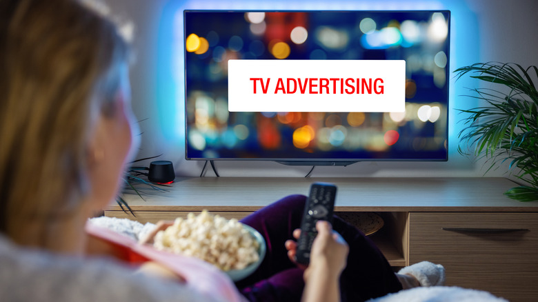 Woman with bowl of popcorn on the couch with a TV remote pointed at TV advertising on television
