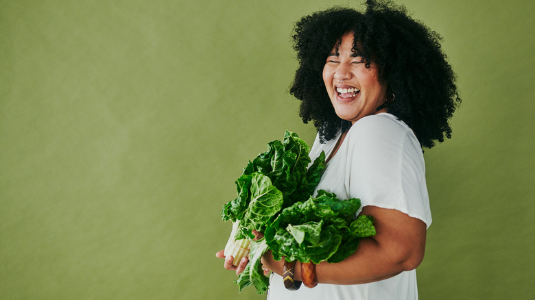 woman smiling as she holds heads of kale