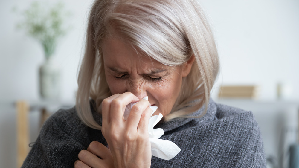 Woman wrapped in a blanket and sneezing into a tissue