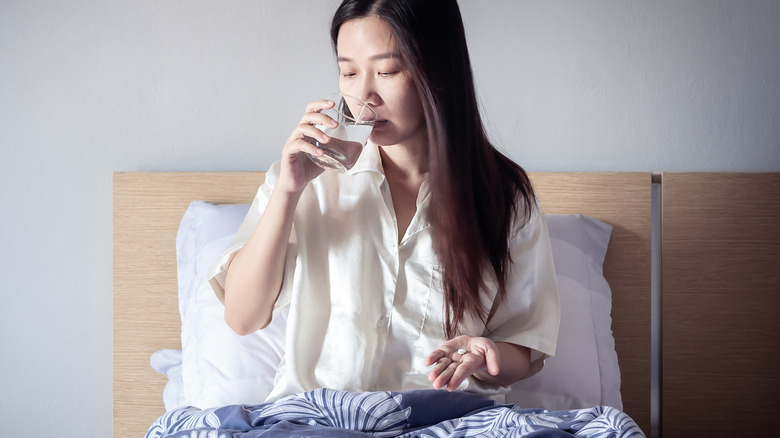 young woman in bed taking pill with glass of water