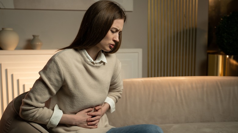 woman on couch holding stomach in pain