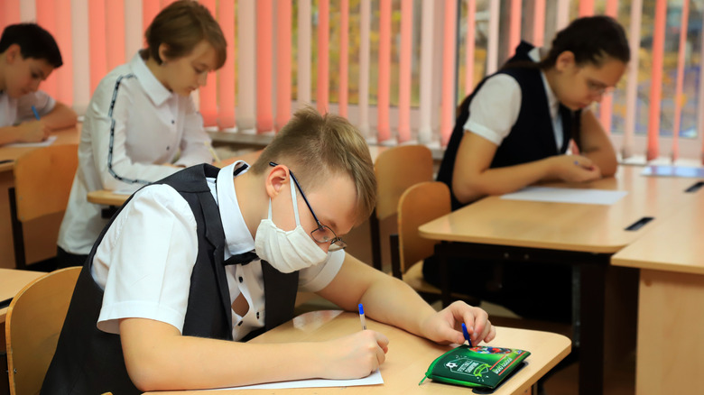 Masked student at desk surrounded by unmasked students studying