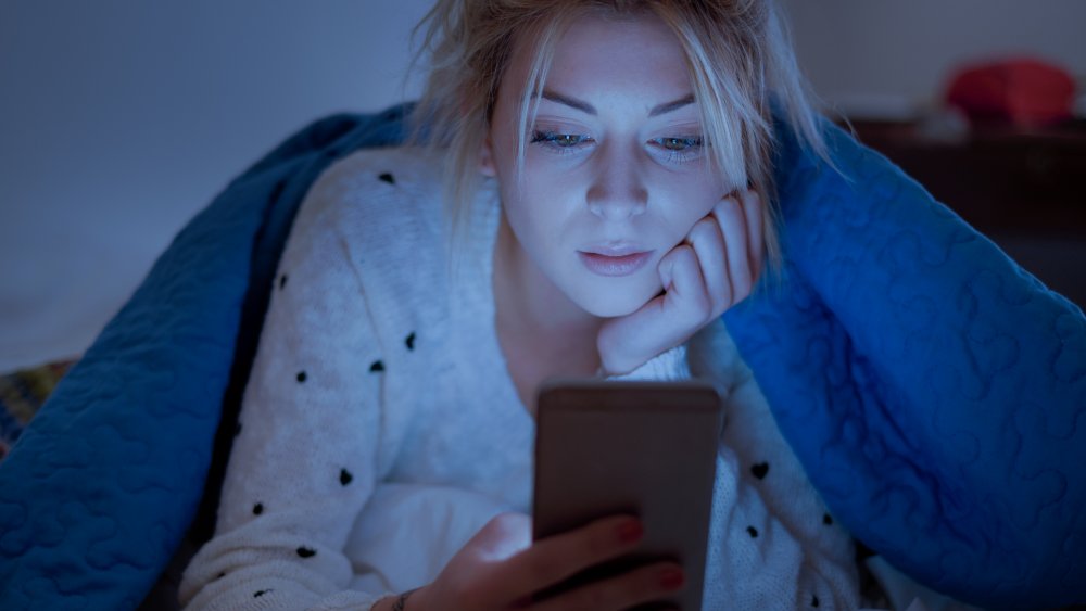 A woman in bed under the covers looking at her phone 