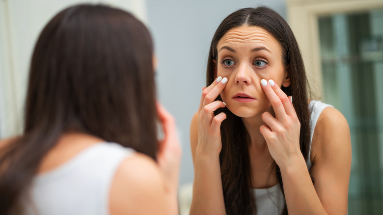 woman checks eyes in mirror