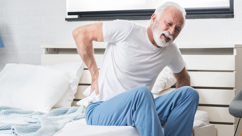 Senior man in pain holding lower back while getting out of bed