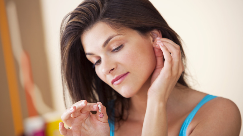 Woman looking at earring in hand and touching her earlobe with the other