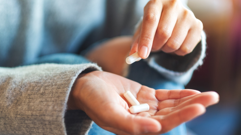 Closeup image of a woman holding white supplement capsules in hand