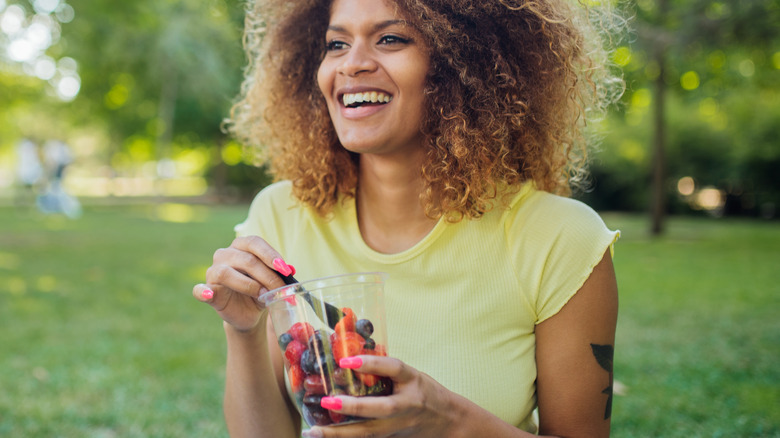 healthy woman eating a cup of berries outside