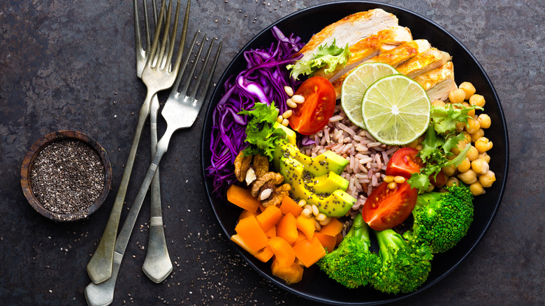 Bowl full of chicken, chickpeas, broccoli, squash, avocado, rice, cabbage and limes