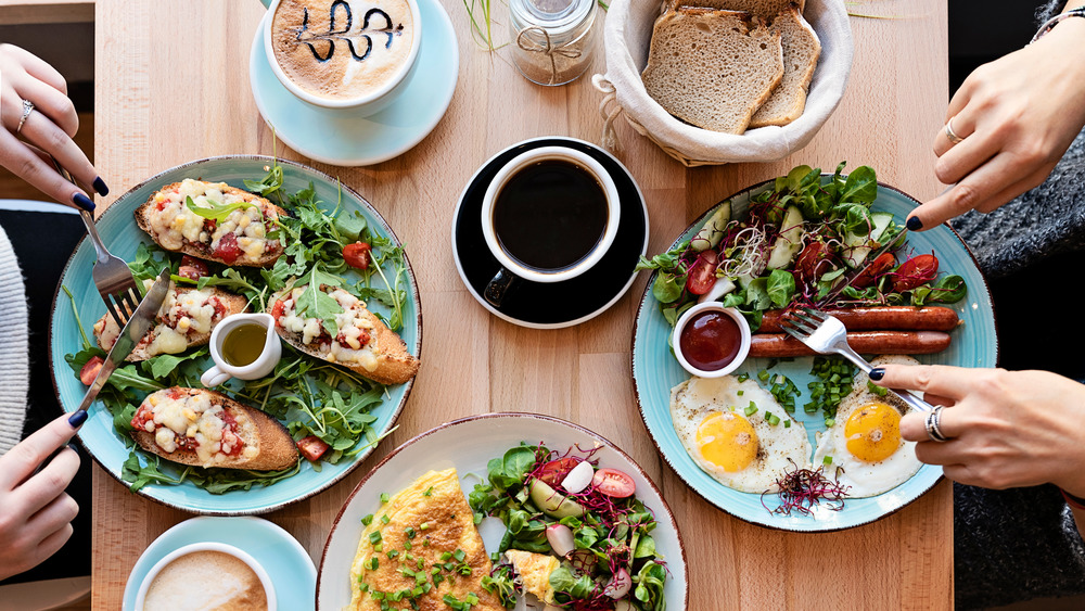 hands using forks and knives on breakfast plates