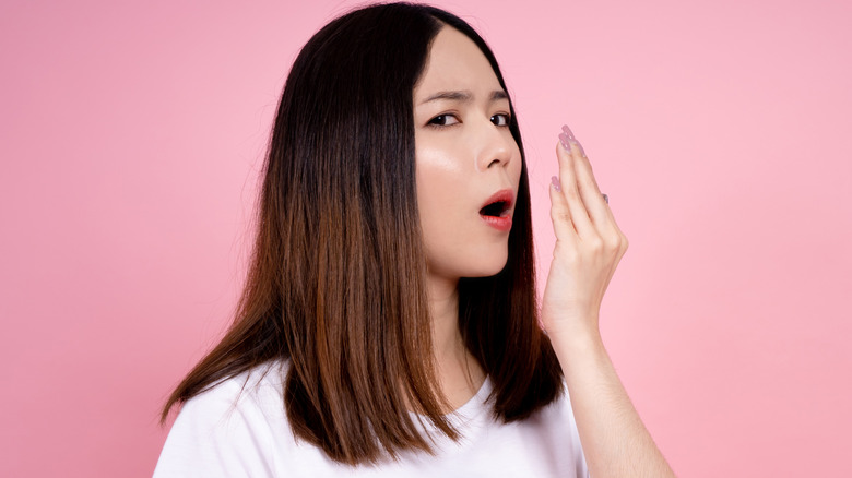 A woman against a pink background checking her breath