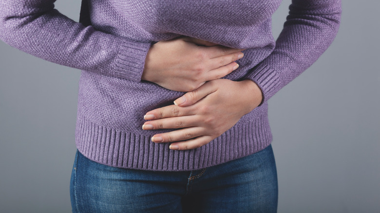 Close up of a woman in a sweater holding her stomach in discomfort