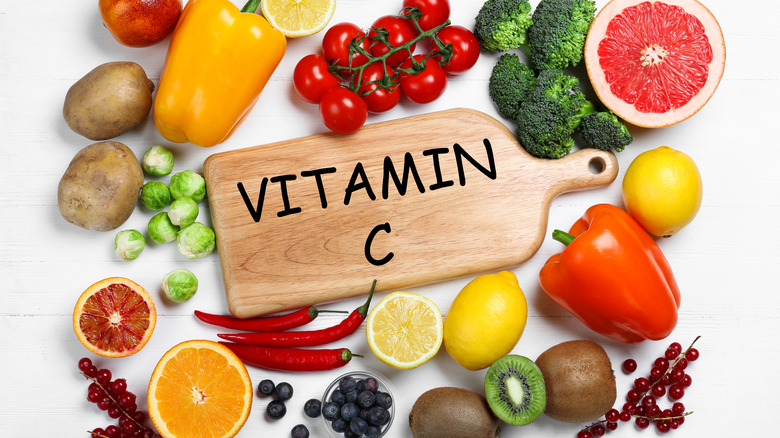 The phrase "vitamin C" written on a wooden cutting board and surrounded by fruits and vegetables