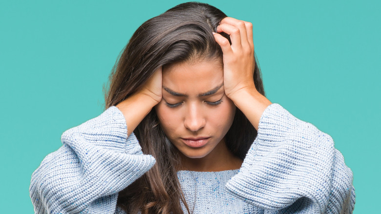 Woman in a light blue sweater holding her head in pain