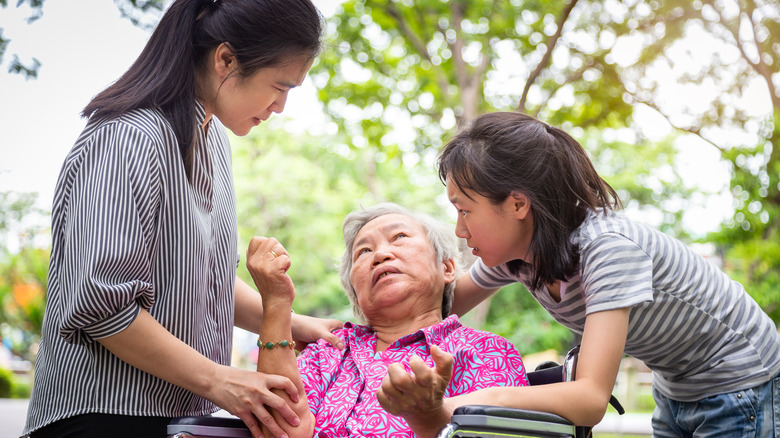Elderly woman in a wheel chair being attended to by a younger woman and a child