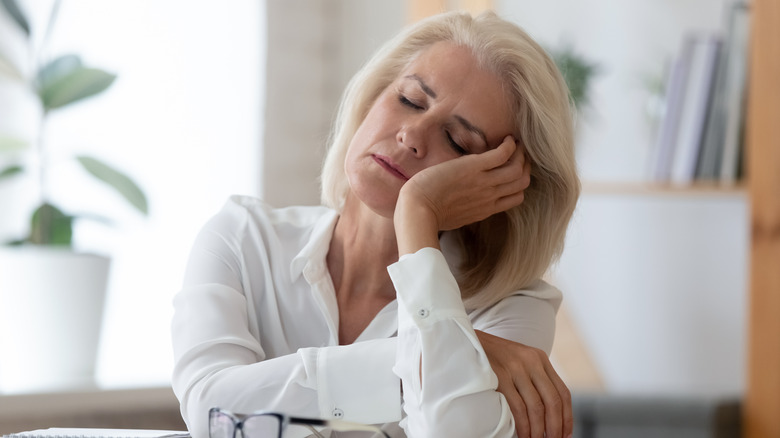 A tired woman in a white dress shirt propping her head up with her hand