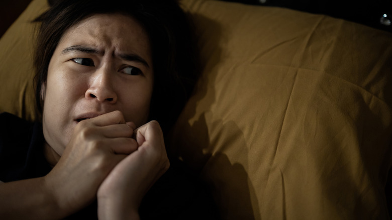 An afraid woman lying in bed looking to her left while agitated