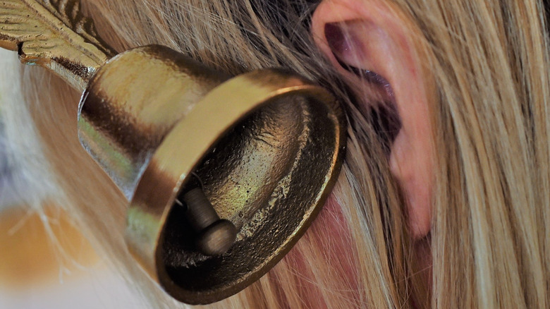 Close up of a bell being held next to a person with sandy blonde hair's ear