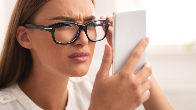 Woman squinting while wearing glasses and looking at a smartphone