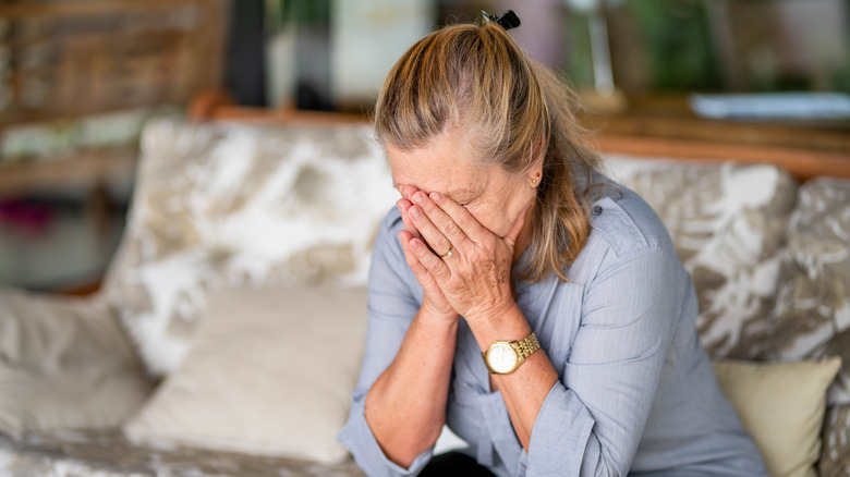 Sad woman sitting on couch with face in hands