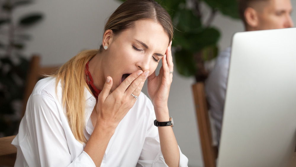 Person sitting at computer with eyes closed yawning