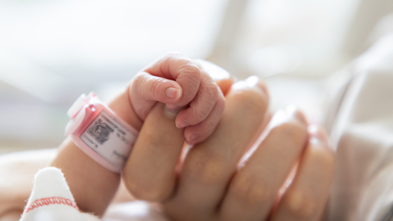 A baby holds its mother's hand